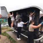 Group of young people being overseen by Duncan painting the shelter with black hammerite